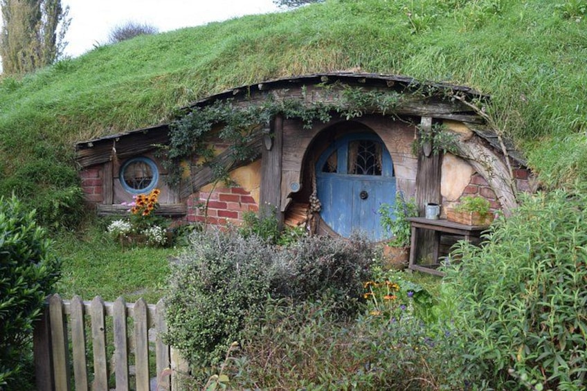 A Hobbit-style house with a blue door, surrounded by lush greenery and a wooden fence. 4