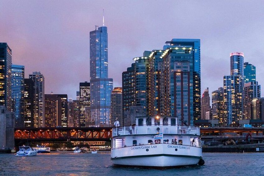 Ein Fluss mit einem Boot namens 'Chicago Classic Lady' und einer Stadtansicht, im Hintergrund hoch aufragende Gebäude. 3
