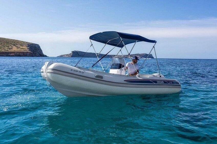 A white motorboat with a blue canopy on calm turquoise waters, a rocky coastline in the background, and a clear sky. 2