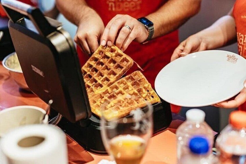 A waffle iron with waffles being removed, a plate, and a bottle of water. 2