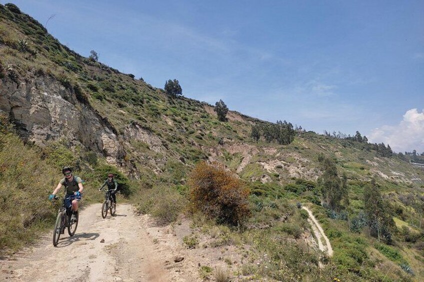 Dos ciclistas en un sendero de tierra rodeados de colinas y vegetación escasa. 3