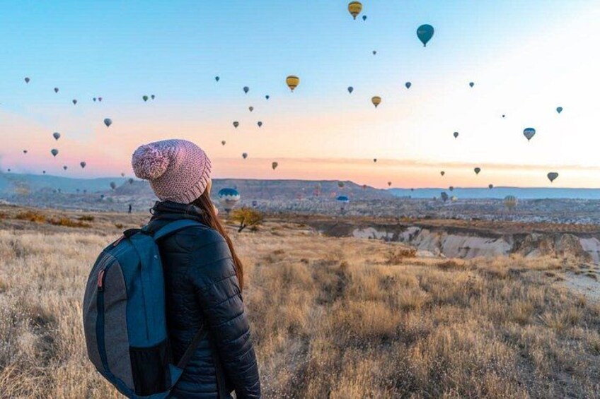 Una persona de pie en una colina con una mochila, mirando globos aerostáticos en el cielo. 3