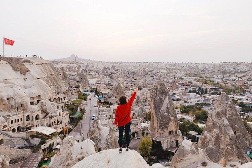 Una persona parada en un afloramiento rocoso con vistas a un paisaje urbano, formaciones rocosas singulares y una bandera. 4