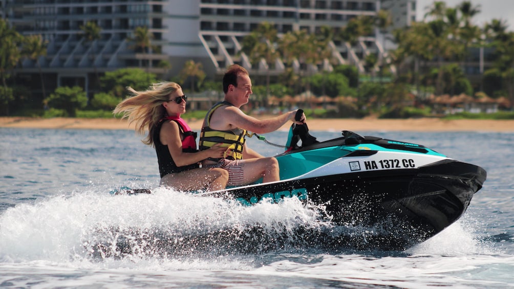 A jet ski with two people on it, moving through water with waves around it. 5