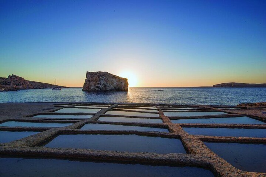 A coastal scene with a rock formation and a boat in the distance during sunset. 2