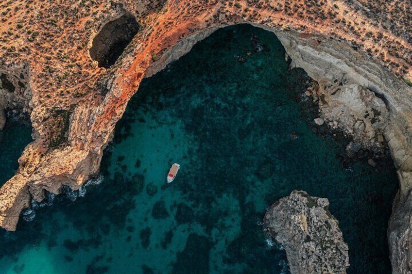 A boat in a clear blue sea, rocky coastline, and a natural arch formation. 4