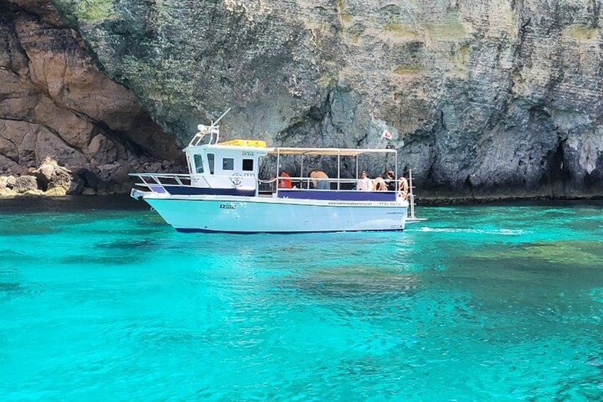A boat with passengers on turquoise water near a rocky cliff. 4