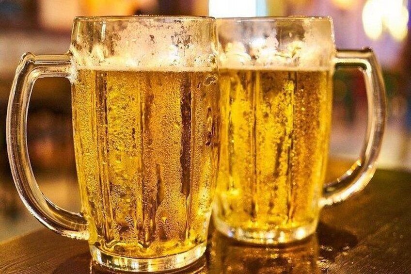 Two glass mugs of beer with handles, filled with a golden liquid, on a wooden surface. 2