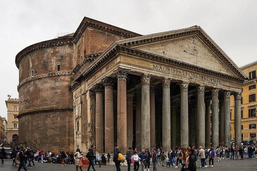 A historic building with columns and inscriptions, surrounded by a crowd of people. 5