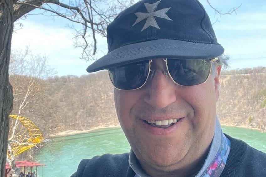 A person wearing a star-patterned cap and sunglasses, with a body of water and a yellow structure in the background. 3