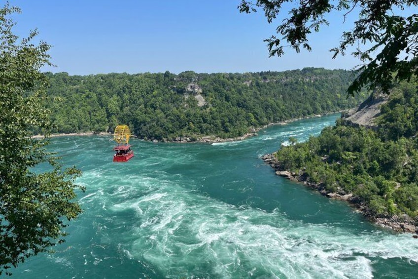 A river with a red boat carrying a yellow canopy, surrounded by dense green forest and a clear blue sky. 5