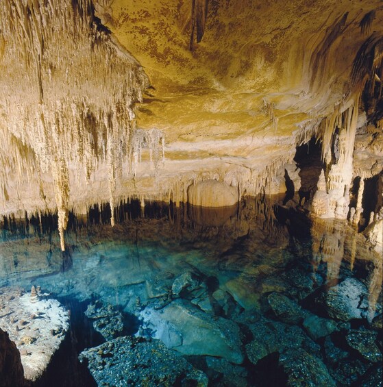 A cave with stalactites and stalagmites, clear water, and rocks. 5