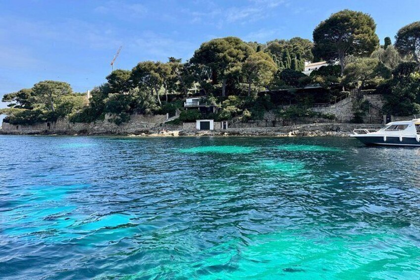 A coastal scene with clear turquoise waters, a boat, and a hillside with trees and buildings. 4
