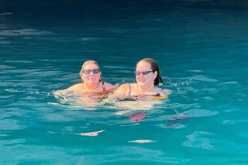 Two people swimming in a clear blue pool. 3