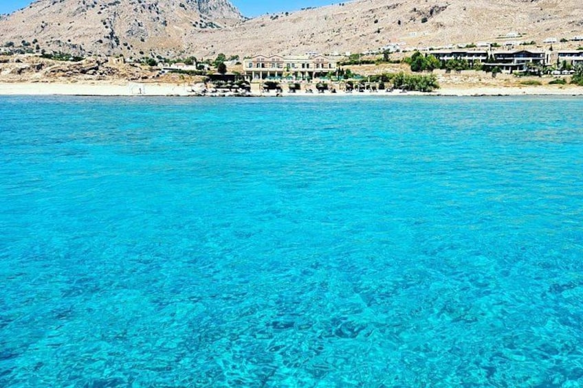 A coastal area with clear blue waters, a mountain in the background, and buildings along the shore. 5
