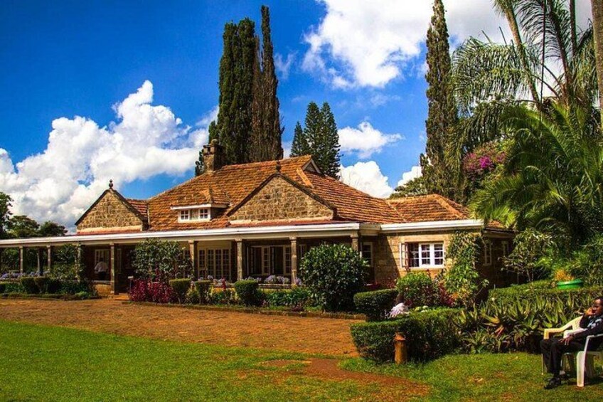 A large stone house with a tiled roof, surrounded by lush greenery and tall trees. 3