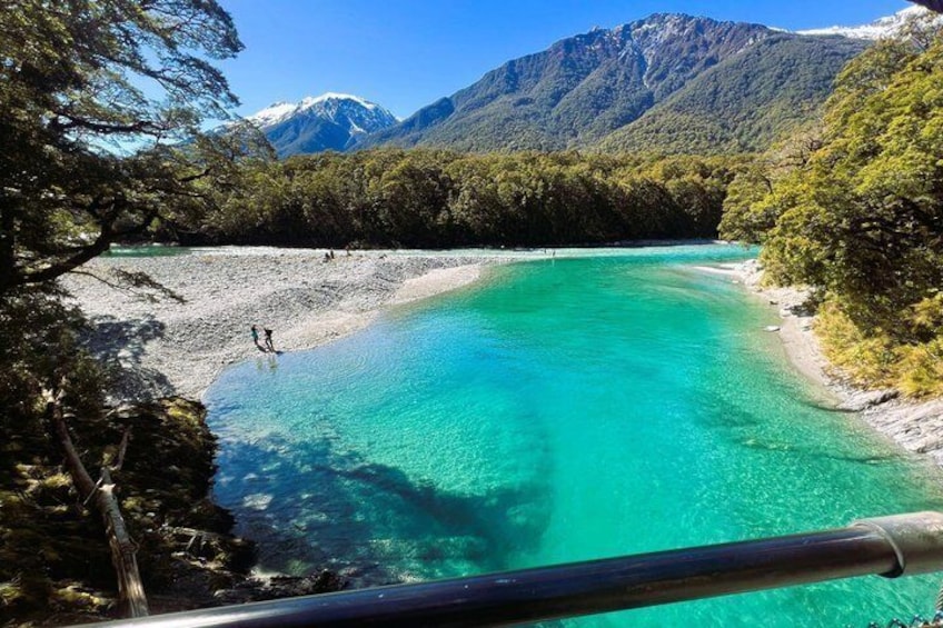 A turquoise lake surrounded by forested mountains and a clear sky. 4