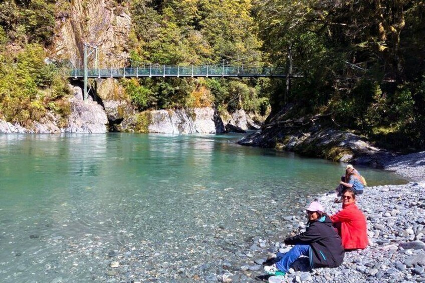 A river with a bridge, rocky shore, and people sitting by the water. 5