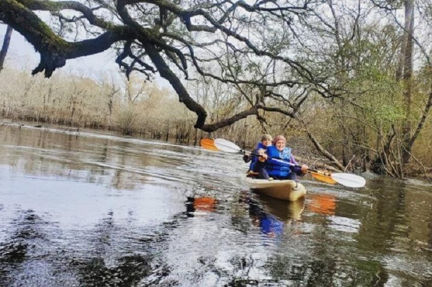 Two people kayaking on a calm river surrounded by trees. 4
