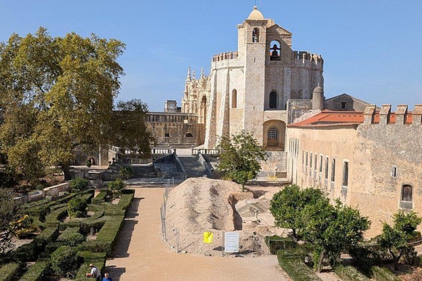 A historic building with a tower, surrounded by a well-maintained garden and a large rock formation. 5