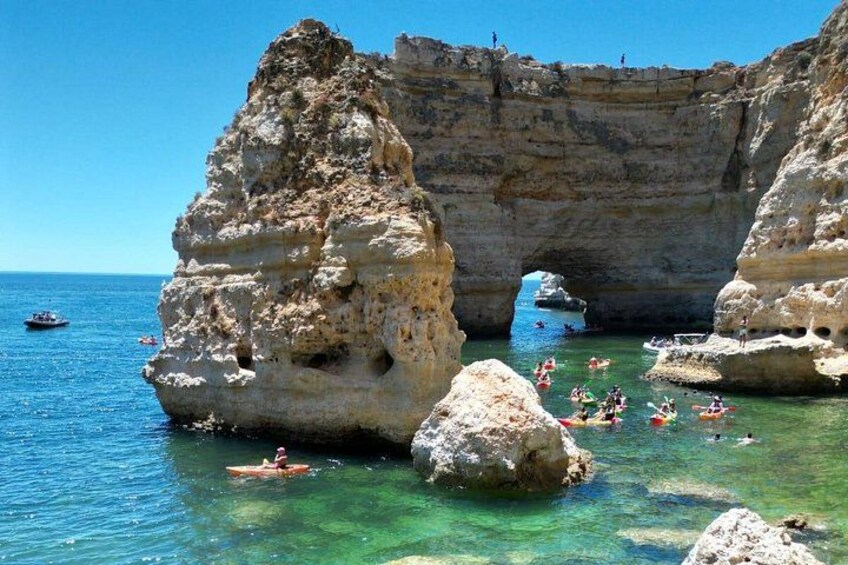 A coastal rock formation with clear water, people kayaking, and a boat in the distance. 3
