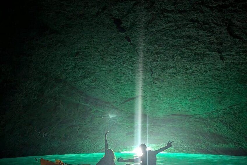 A cave with a greenish glow, a person with raised arms, and a light beam. 4