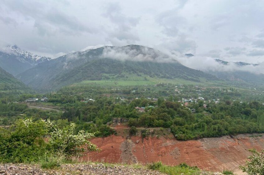 A mountainous landscape with a village nestled in the valley, surrounded by greenery and red earth. 2
