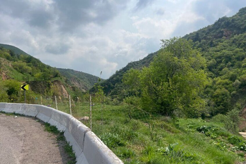 A curving road with a yellow warning sign, surrounded by lush green hills and a cloudy sky. 3
