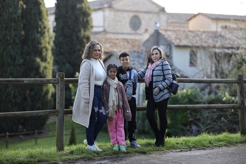 A family of four standing by a wooden fence with a church and greenery in the background. 4