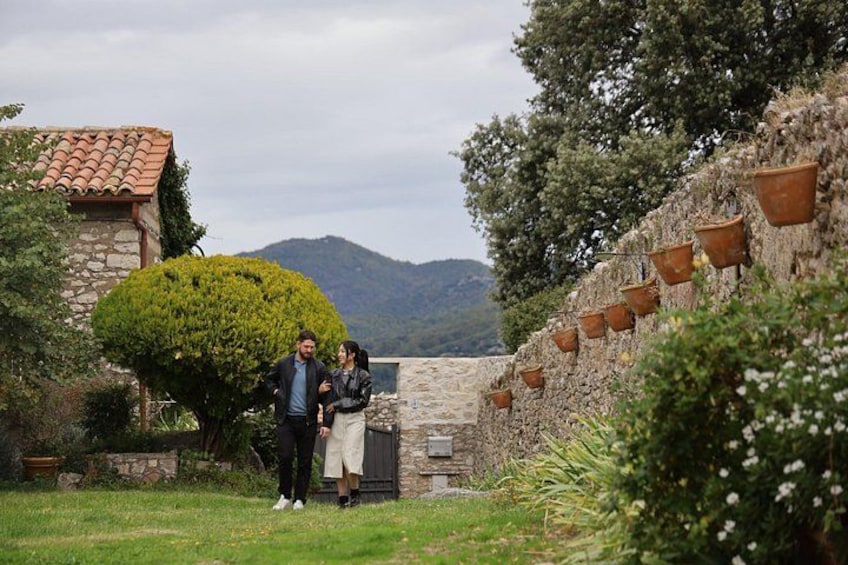 A stone building with a tiled roof, a well-maintained hedge, and a mountainous backdrop. 1