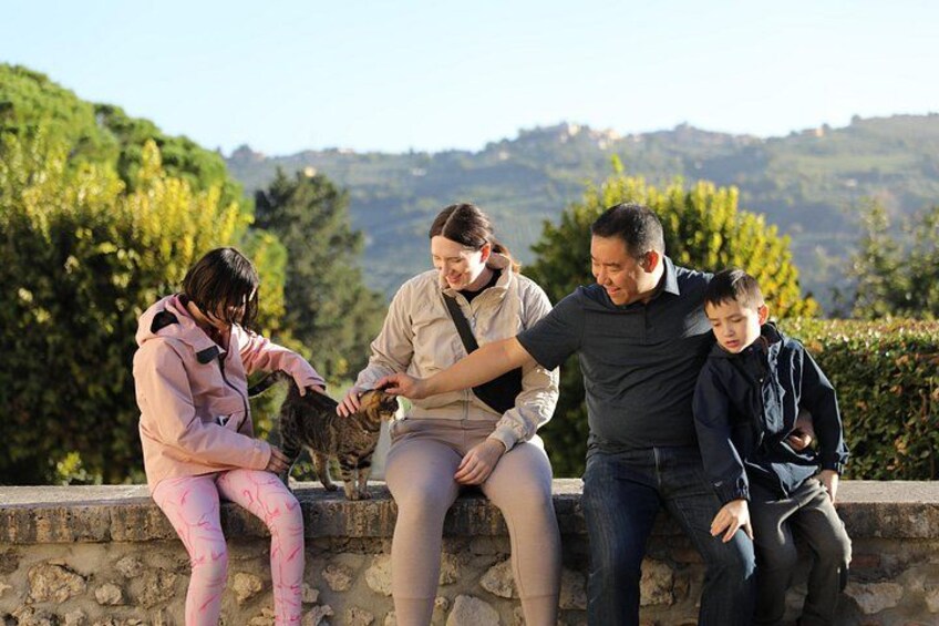 A family of four sitting on a stone wall outdoors with a mountainous landscape in the background. 5