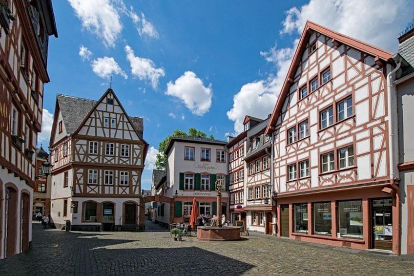 A cobblestone street lined with traditional half-timbered buildings, a clear blue sky, and a few people walking. 1