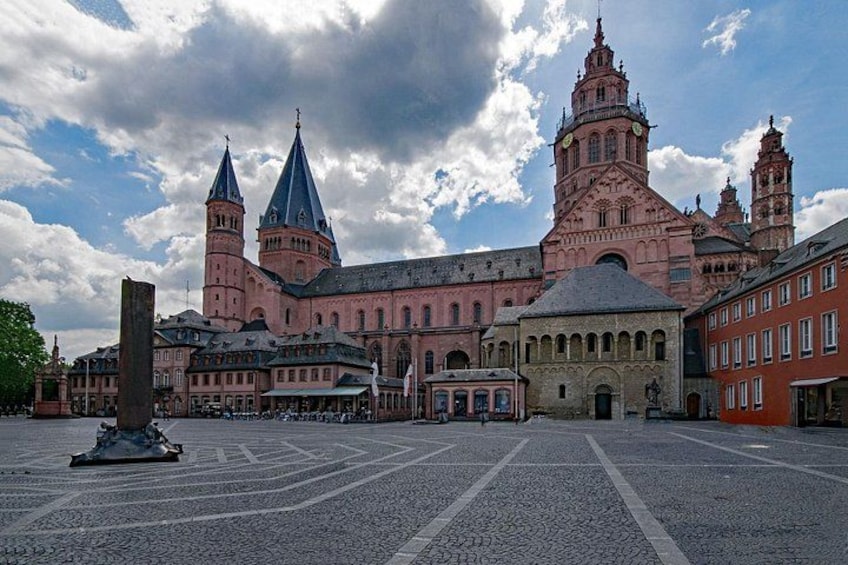 A historic building with two prominent towers, a courtyard, and surrounding architecture. 1