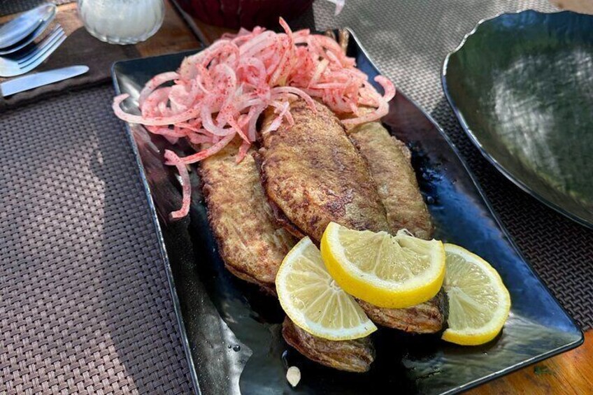 A plate with fried fish, lemon slices, and pickled onions. 4