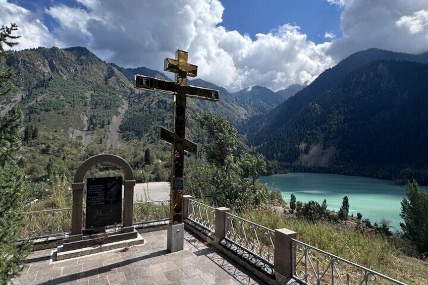 A cross at a mountain overlook with a lake and forested hills in the background. 1