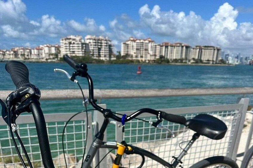 A bicycle with a black seat and handlebars, a yellow front suspension, and a black rear wheel, parked near a waterfront with buildings in the background. 4