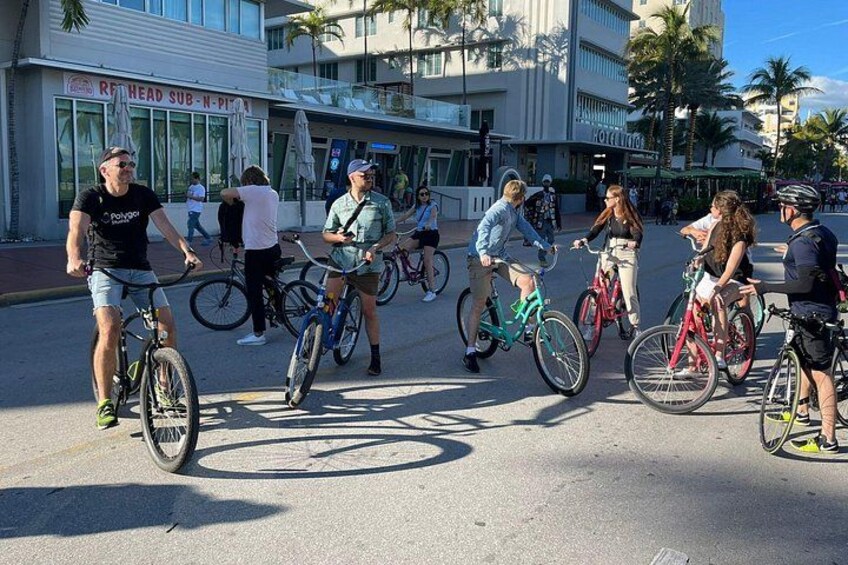 A group of cyclists on a street with palm trees and a building in the background. 5