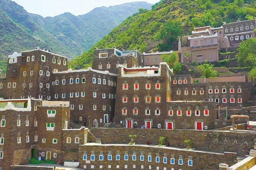 A cluster of traditional buildings with red and white doors, set against a backdrop of lush green hills. 4
