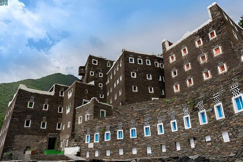 A multi-story stone building with a green door and blue window frames. 3
