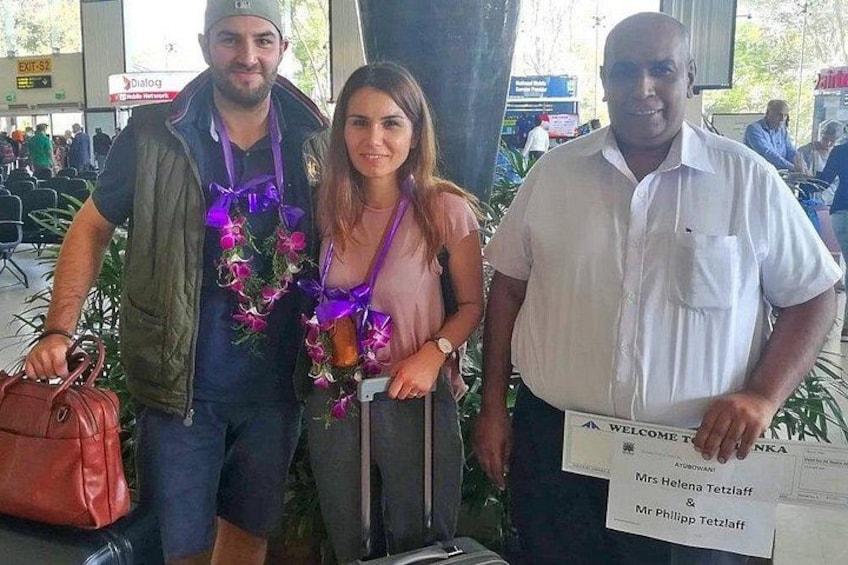 Tre personer står i en lufthavn og holder en velkomstplakát. 1