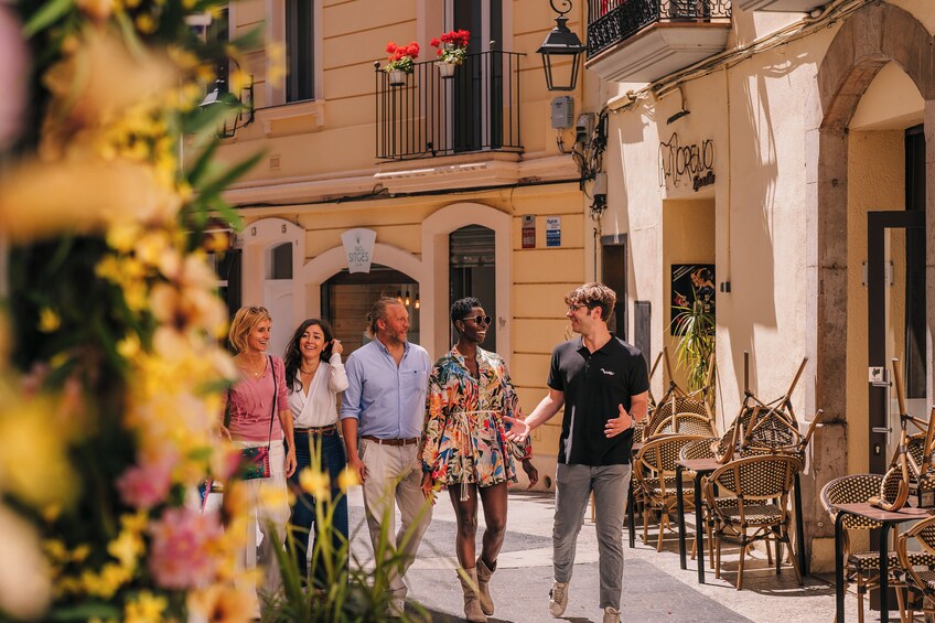 A group of people walking on a street with outdoor seating and flowers in the foreground. 2