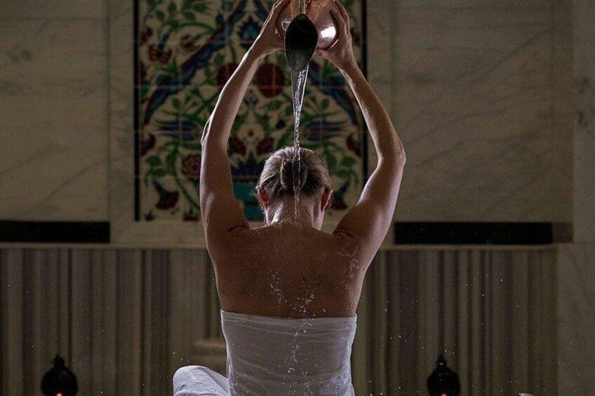 A person in a white garment performing a water ritual in a room with a decorative wall. 5