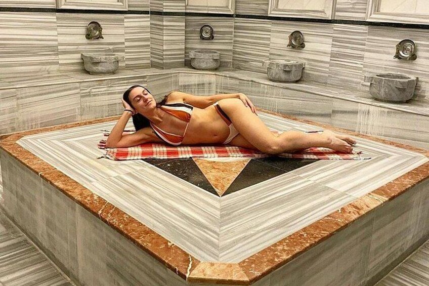 A person lying on a checkered towel in a bathtub with a marble surround. 3