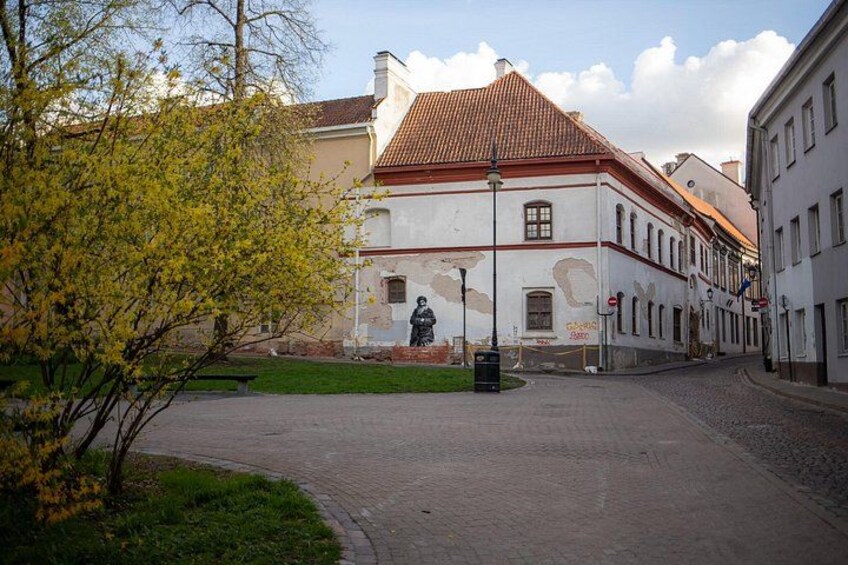 En kullerstensgata med en byggnad som har ett rött tegeltak och en staty framför sig. 4