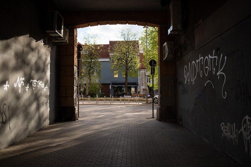 En stadsgata under en bro, med graffiti på väggarna och en byggnad i bakgrunden. 1