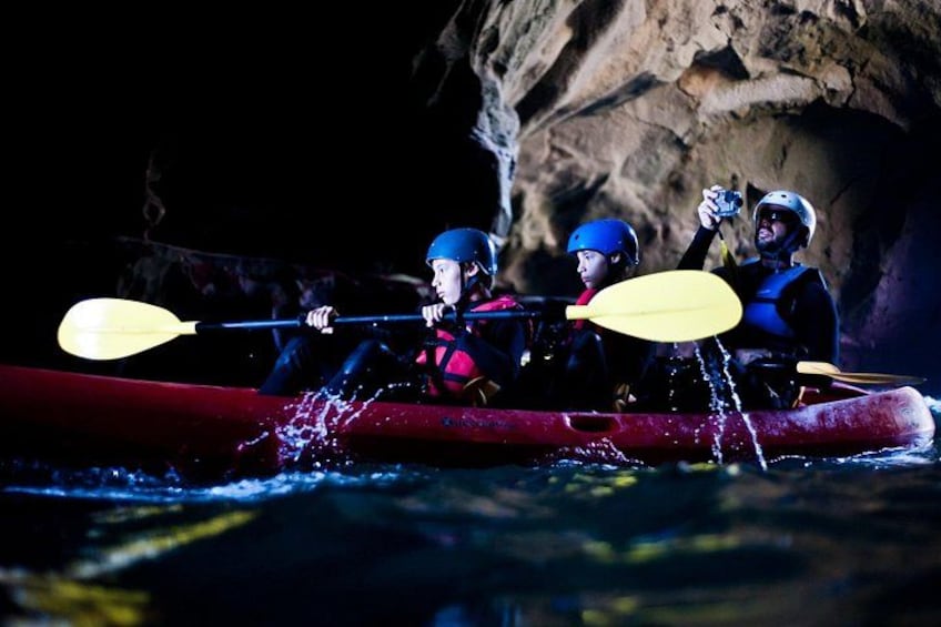 A group of kayakers in a red kayak navigating through a water body with a rocky cave in the background. 2