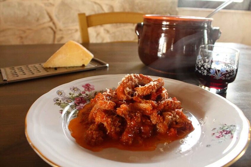 Een bord met gehaktballetjes in tomatensaus, een rasp, een rode pan en een glas rode wijn op een tafel. 1