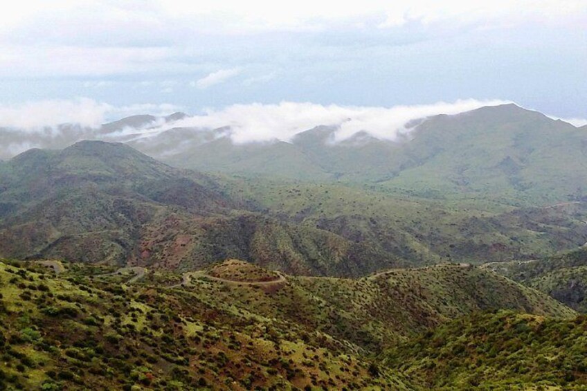 Un paysage montagneux avec des collines ondoyantes, une route sinueuse et un sommet lointain enveloppé de brume. 5