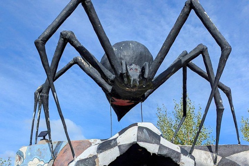 Eine große Spinnenskulptur mit einem menschlichen Gesicht auf dem Rücken, montiert auf einer Felsformation. 4