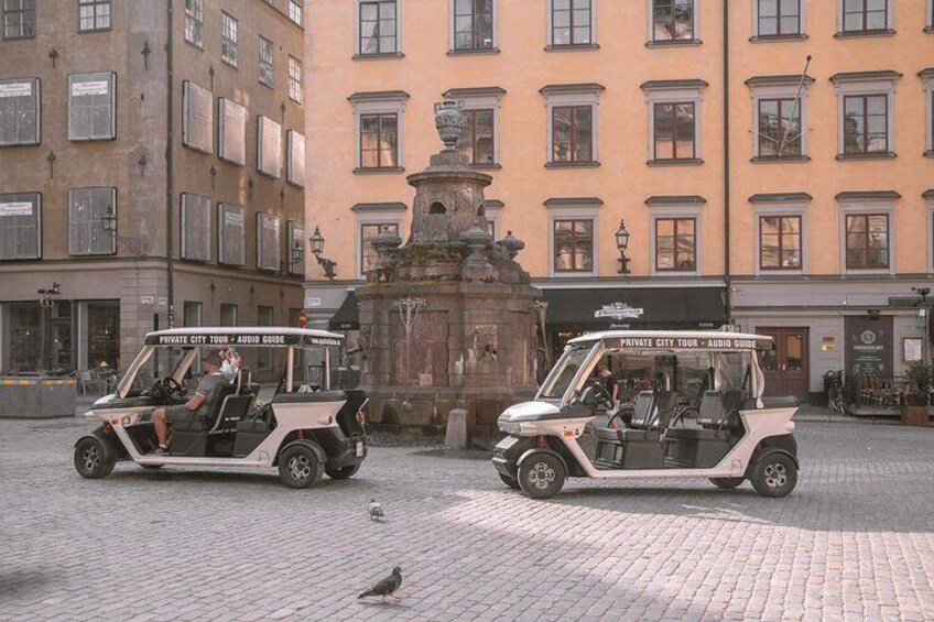 Two golf carts parked on a cobblestone street with buildings in the background. 3